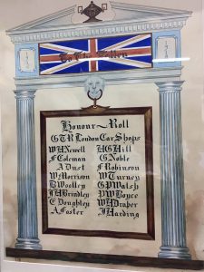 A Roll of Honour including 16 names in a rectangular shape. The shape is surrounded by elaborate neoclassical decorative architecture with a union jack flag superimposed by the inscription "To the Fallen."