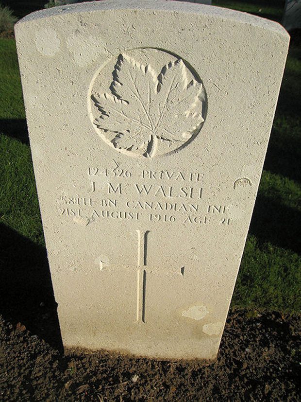 A grave stone with a cross and a maple leaf.