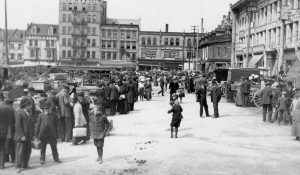 Photograph of people at the market, children playing and buildings.