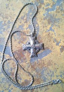 Une croix grecque en argent. Un chiffre se trouve à l’intersection des bras, des feuilles d’érables et une couronne à l’extrémité des bras de la croix. Elle est suspendue à une chaine en argent par un anneau.