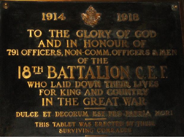 Detail of a plaque with golden lettering on dark background showing the badges of 18 Battalion CEF.