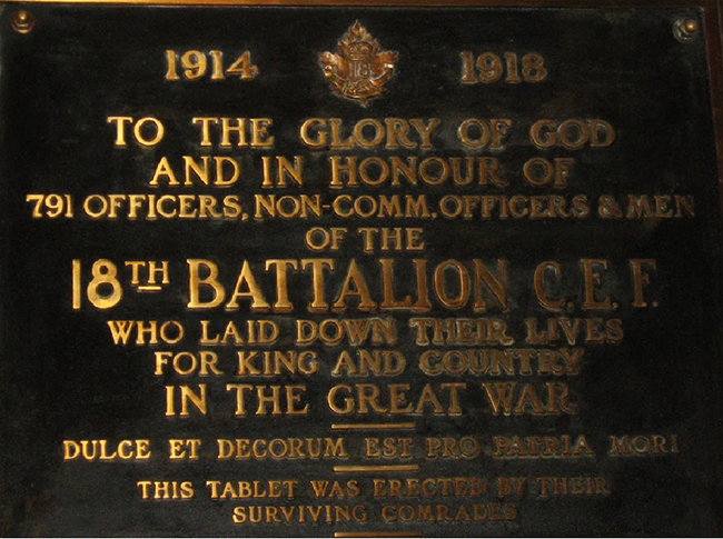 Detail of a plaque with golden lettering on dark background showing the badges of 18 Battalion CEF.