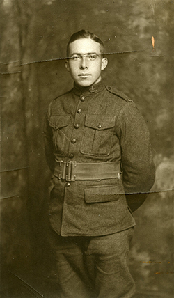 A soldier holding his arms behind his back, he wears a belt on his waist, chest pockets and lower pockets can be seen.