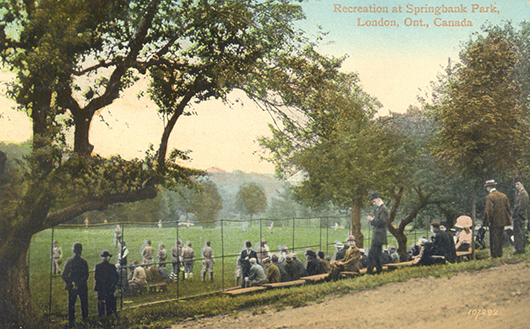 Postal card in colour, showing a group of people watching a sports game in a park.