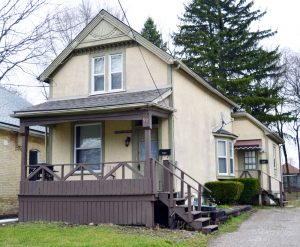 Une maison familiale à deux étages pourvue d’un porche devant l’entrée principale (la porte est sur la gauche) et d’un escalier sur le côté. Il y a une autre entrée derrière, pourvue d’une rampe d’escalier.