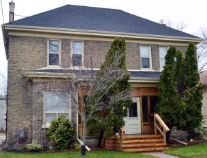 A 2 storey house, stairs to front door in centre. Bushes and trees in front of the house.