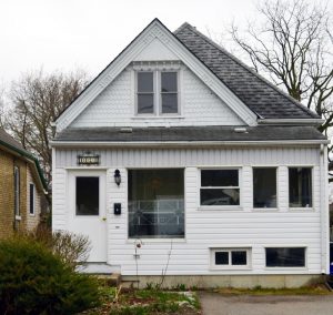 Une maison à un étage et demi, dont la porte d’entrée est située sur la gauche. Une forme triangulaire avec une fenêtre surmonte la façade.