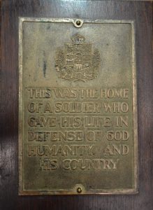 A rectangular brass plaque with coat of arms and the inscription "This was the home of a soldier who gave his life in defense of God, humanity and his country".