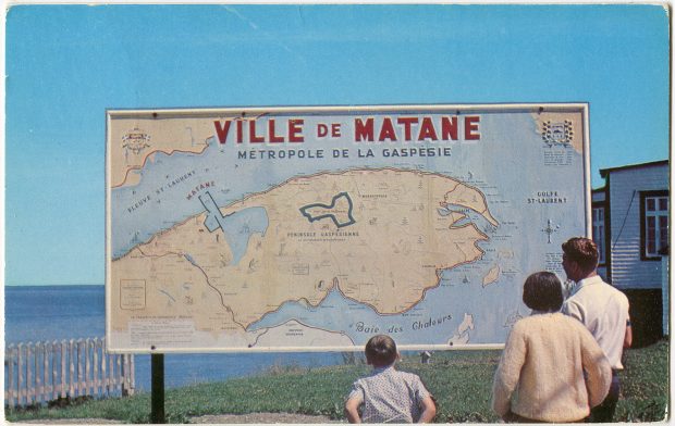 A man, a woman and a child observe a map of the Gaspésie. The map is approximately 4 feet high by 8 feet wide. Located outdoors near the Matane lighthouse, it reads: Ville de Matane ‘Métropole de la Gaspésie.