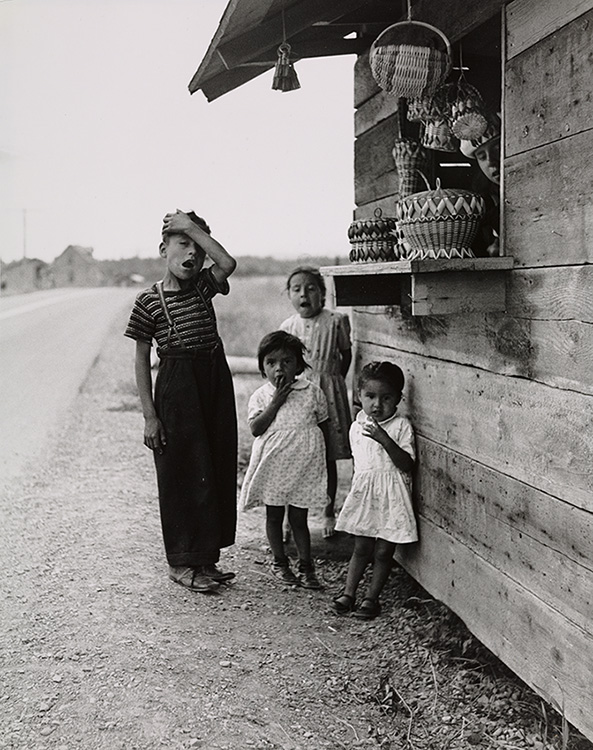 Black and white portrait of four Mi'gmaq children in front of a roadside kiosk selling basketry.