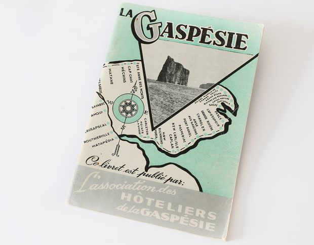 Cover of a tour guide La Gaspésie is drawn in black and white on a pastel green background representing the St. Lawrence River. All villages along the route of Route 6 have been identified. In the top, La Gaspésie is written in big letters. Below, a photograph of Percé Rock is presented in a triangular shape. At the bottom of the page is written This booklet is published by l’Association des Hôteliers de la Gaspésie.