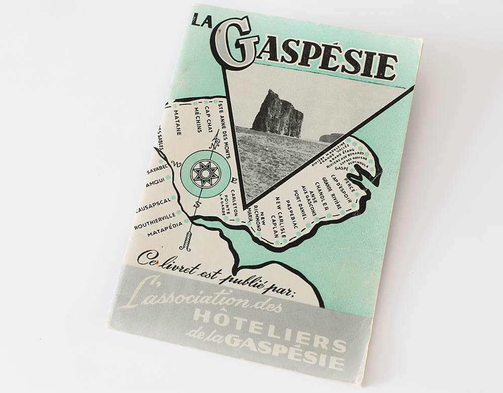 Cover of a tour guide La Gaspésie is drawn in black and white on a pastel green background representing the St. Lawrence River. All villages along the route of Route 6 have been identified. In the top, La Gaspésie is written in big letters. Below, a photograph of Percé Rock is presented in a triangular shape. At the bottom of the page is written This booklet is published by l’Association des Hôteliers de la Gaspésie.