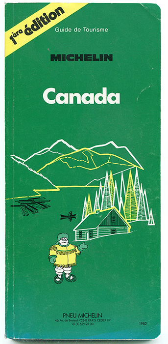 Cover of the first edition of the Michelin Guide. On a green forest green background, the Michelin tire mascot is wearing a coat with bangs. He is wearing snowshoes and a fur hat. Behind him is a log cabin in an evergreen forest near a lake on which there is a canoe and logs. In the background, a chain of mountains.