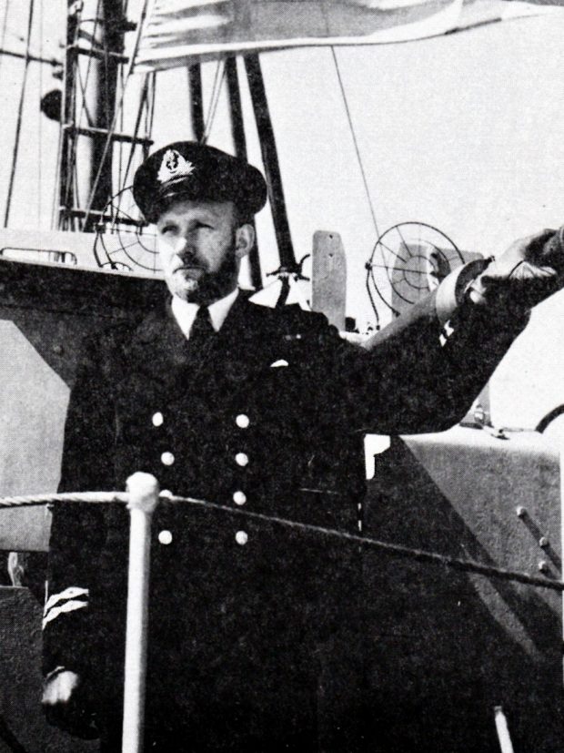 Navy officer standing beside deck gun on warship