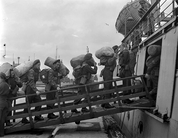 soldiers board a ship carrying duffle bags