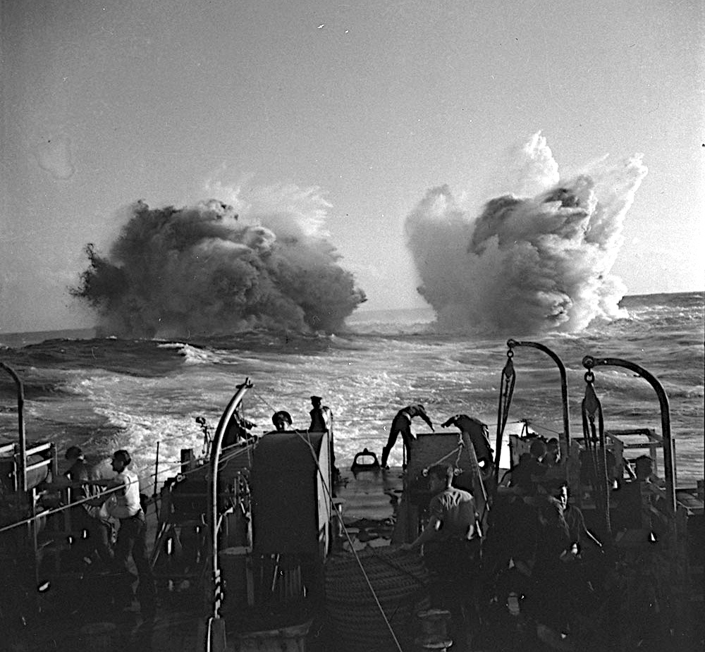 Two depth charge explosions behind a warship