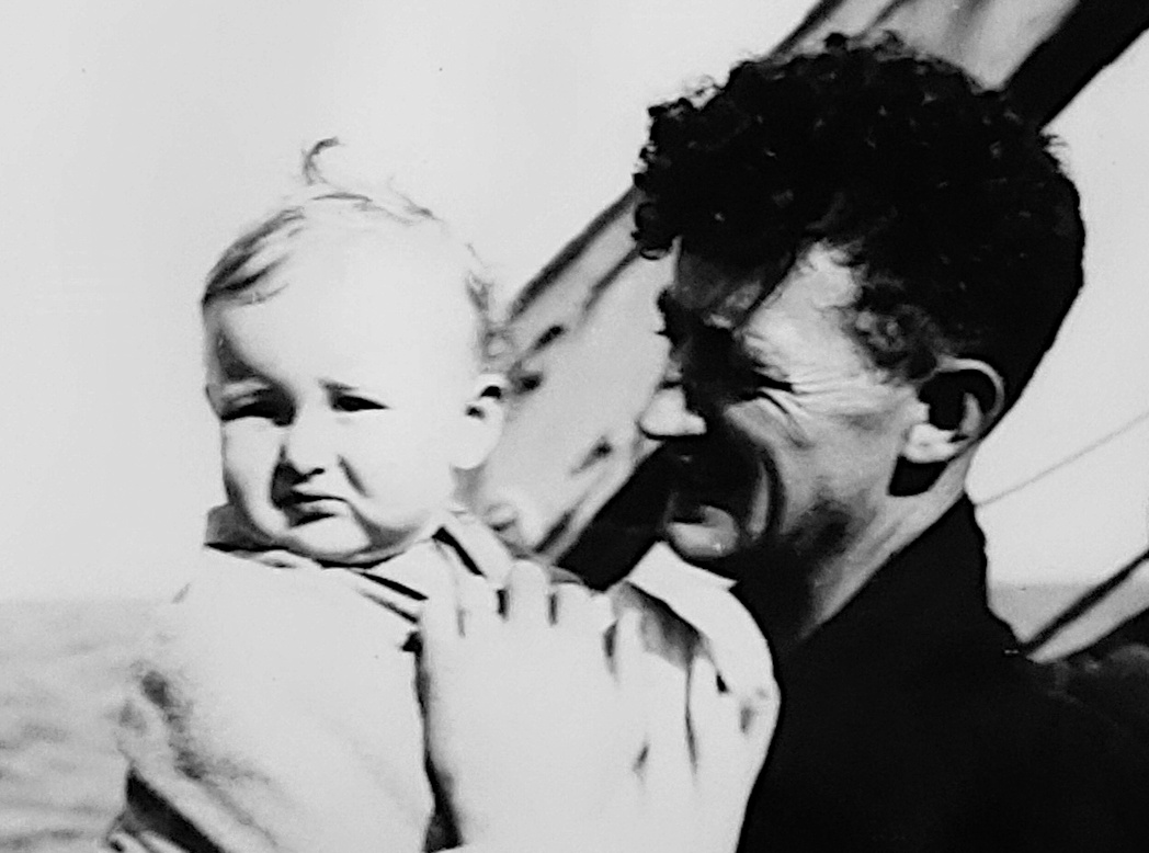 A man holds a baby on the deck of a ship