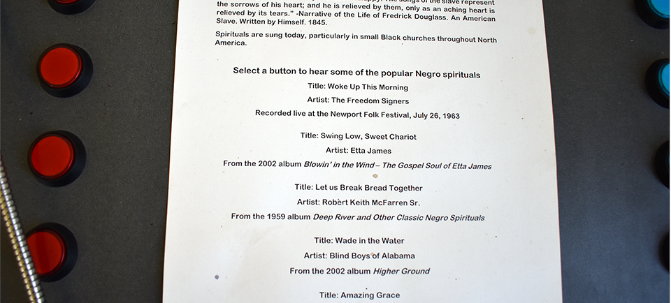 Interactive display page titled 'Songs of the Enslaved' with historical context about Negro spirituals and five red buttons to play different spiritual recordings.