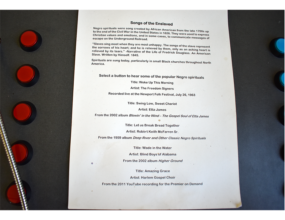 Interactive display page titled 'Songs of the Enslaved' with historical context about Negro spirituals and five red buttons to play different spiritual recordings.