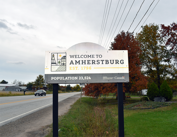 Welcome sign for Amherstburg, Ontario, established 1796, population 23,524, with trees showing autumn foliage in background.