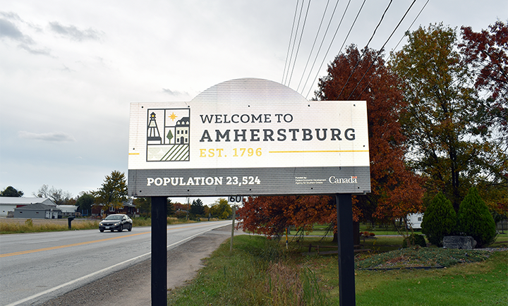 Welcome sign for Amherstburg, Ontario, established 1796, population 23,524, with trees showing autumn foliage in background.