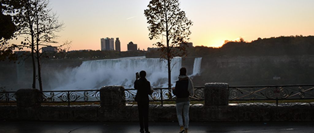Two researchers standing near a railing at sunrise, overlooking Niagara Falls with mist rising in the distance.