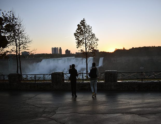Two researchers standing near a railing at sunrise, overlooking Niagara Falls with mist rising in the distance.