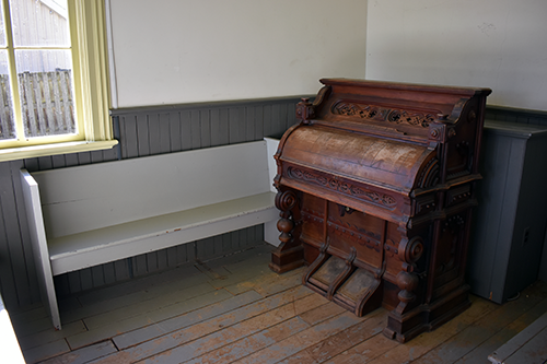 The original church organ inside the Pioneer Church at the Josiah Henson Museum of African-Canadian History. The ornate wooden organ sits in the corner beside simple wooden pews and painted walls. Photo by Blessing Ogunyem