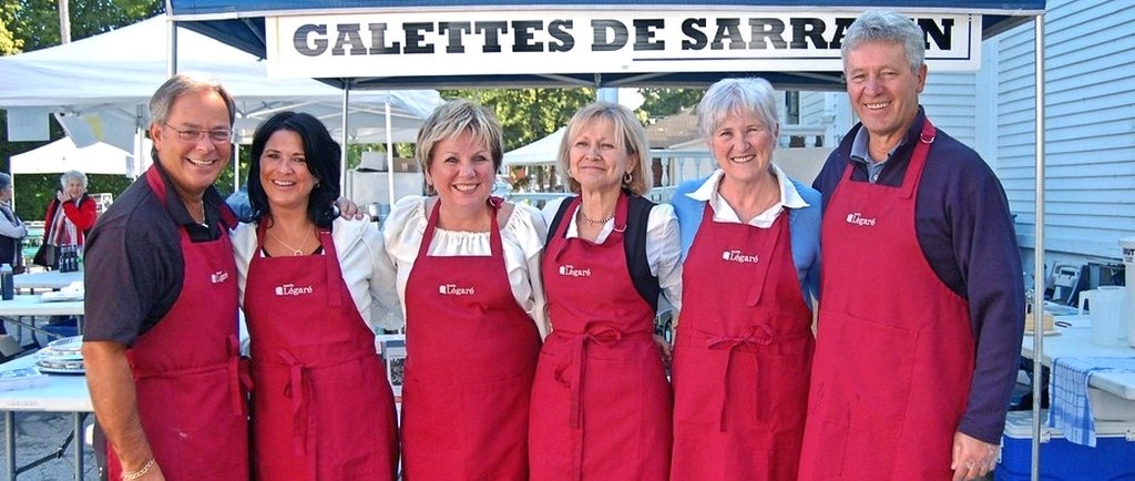 Wide shot of six people wearing red aprons standing in front of a tent where galettes de sarrasin (buckwheat crêpes) are sold.