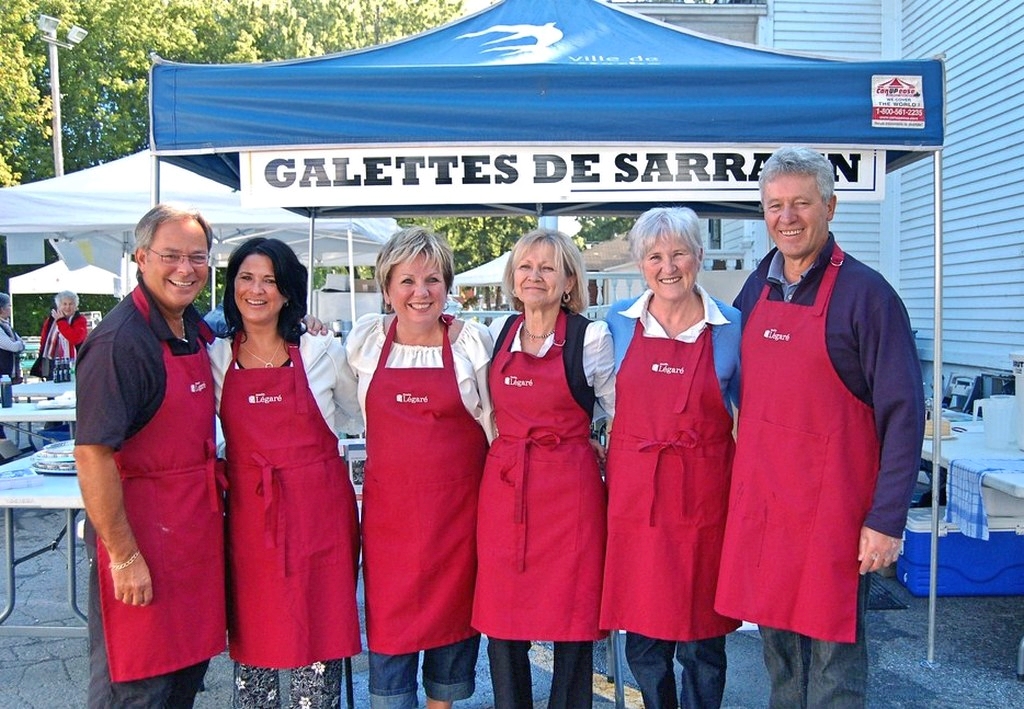 Wide shot of six people wearing red aprons standing in front of a tent where galettes de sarrasin (buckwheat crêpes) are sold.