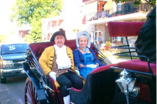 Ernest Labelle, wearing a three-cornered hat, and Marthe Beausoleil, wearing a bonnet, seated in a buggy.