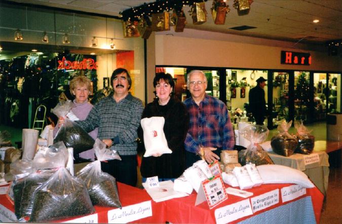 Four volunteers stand behind a table holding flour bags in this photo taken at a shopping mall decorated for Christmas.