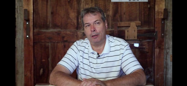 Bust shot of Daniel Saint-Pierre with short hair, wearing a white polo shirt with black stripes, sitting in front of a wooden door.