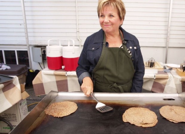 Waist-up shot of Nicole Carignan Lefebvre with short blonde hair, wearing a green apron and holding a spatula over a griddle.