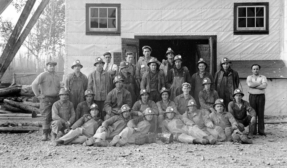 Black and white picture of mine employees in work clothes and gathered before a building.