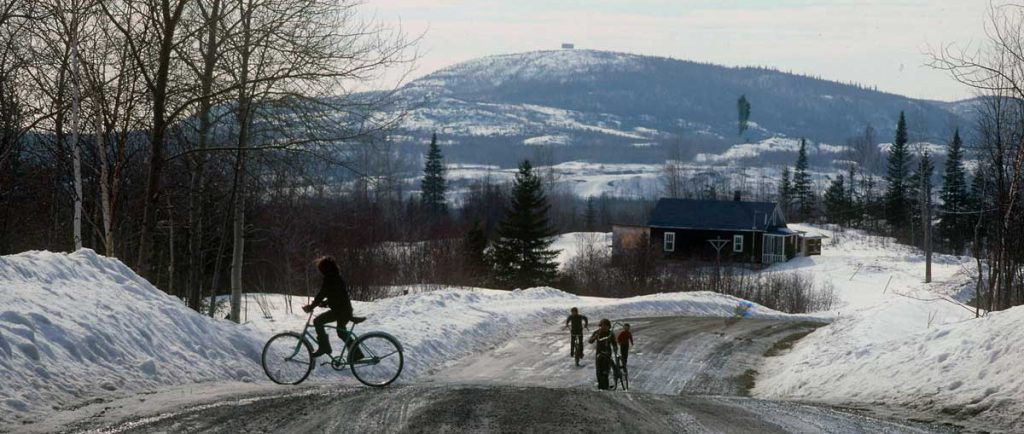 View of a landscape and a rural road in spring during the snow melt. Children riding their bikes.