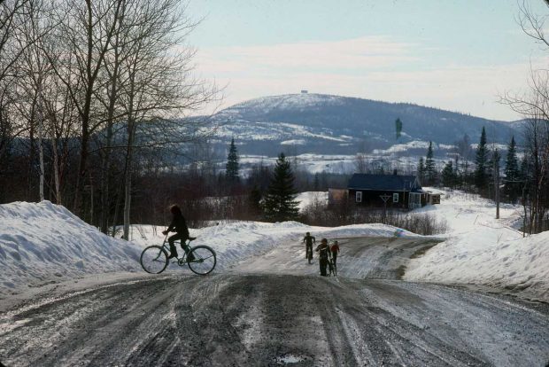View of a landscape and a rural road in spring during the snow melt. Children riding their bikes.