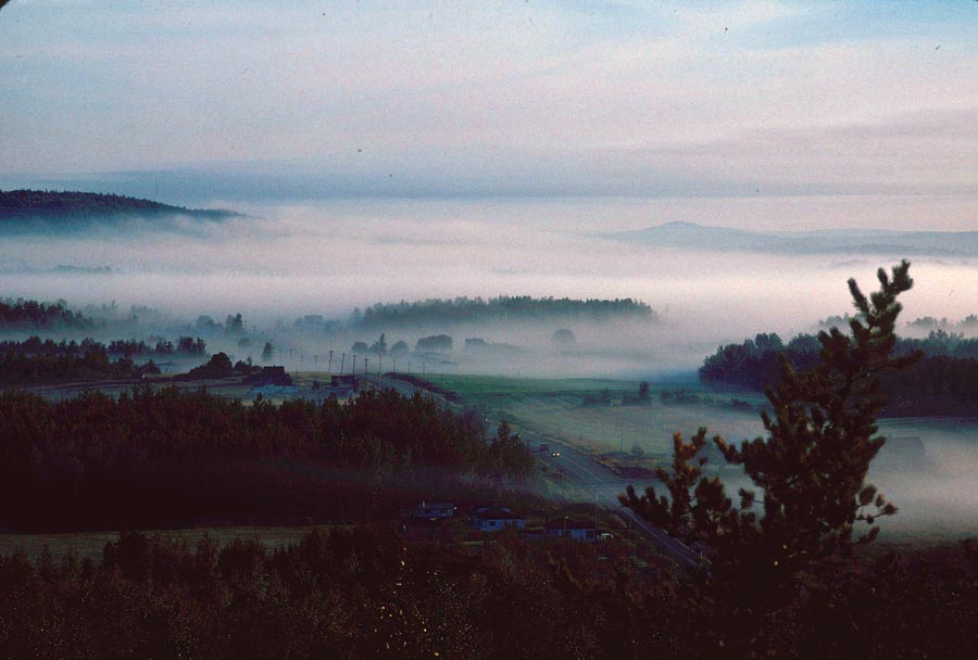 View from a foggy landscape. In the centre, the village from which we can see a few buildings, crossed by a road.