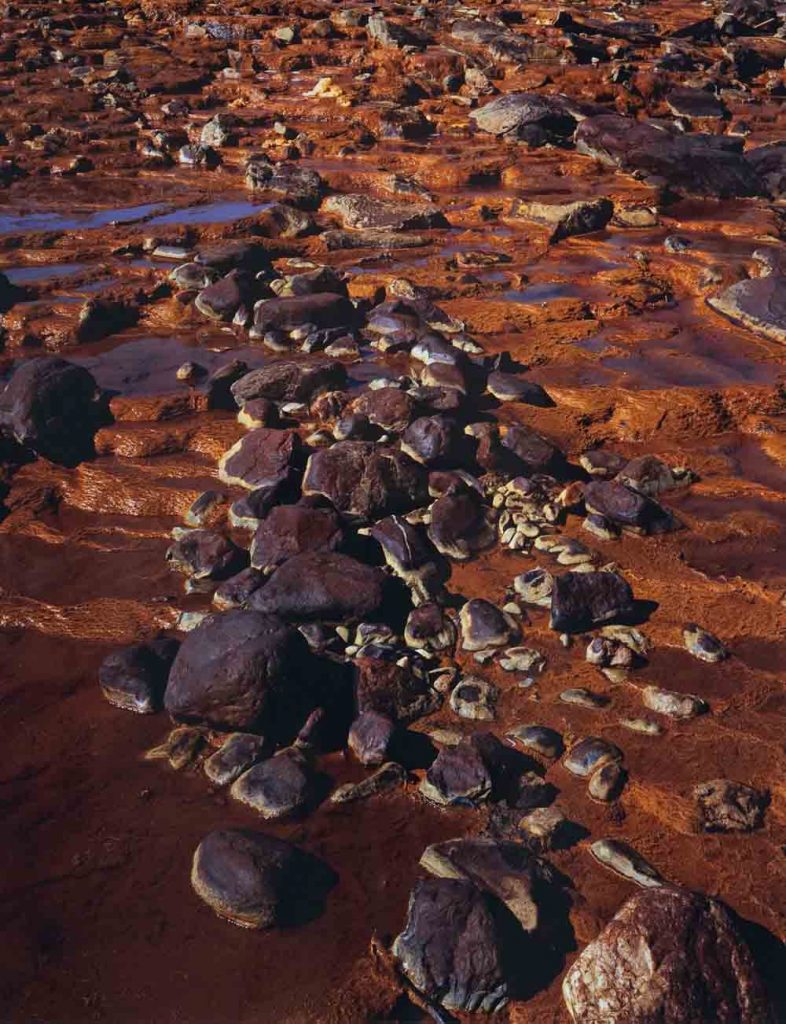 Art picture of a rust-coloured ground with violet rocks and little puddles of water.