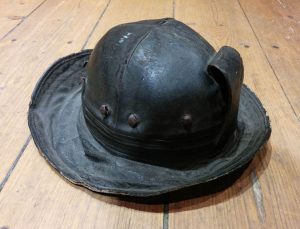 Helmet with a large rim, cracked. An exterior metal hook and a strap.