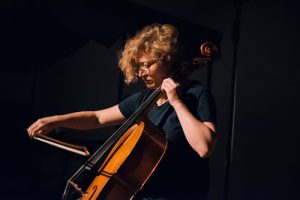Photograph of a female musician playing cello during a musical performance.