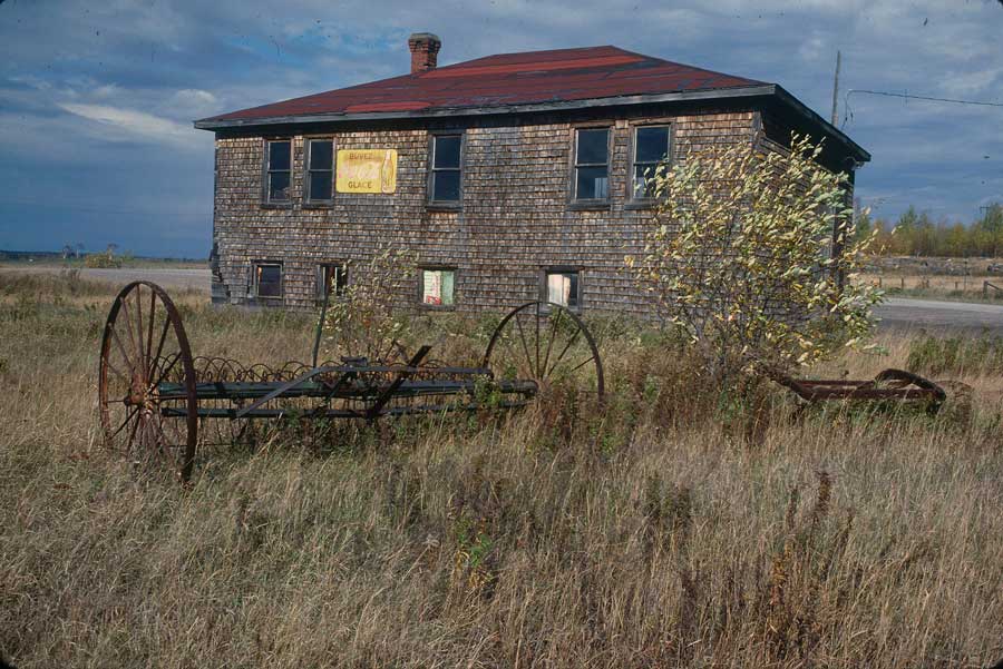 Photographie couleur d'un édifice en bois et de l'équipement agricole abandonné.