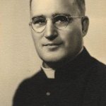 Photographie noir et blanc : un portrait officiel d'un homme en habit de curé, portant des lunettes.