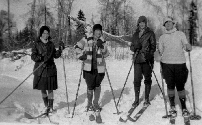 Black and white picture of 4 women cross-country skiing during winter in the forest.