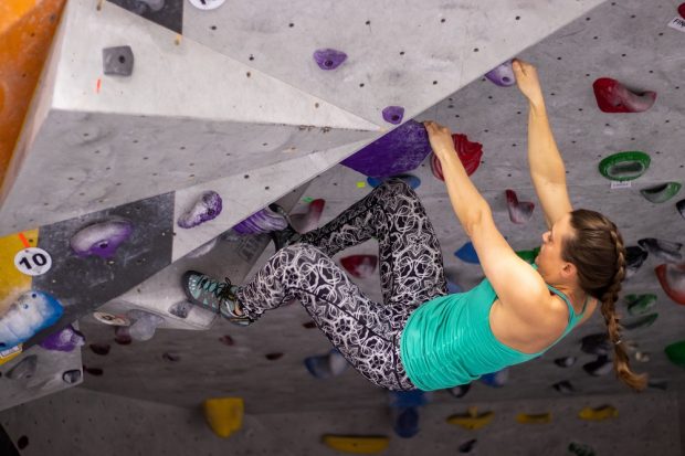 A young woman using hands and feet to hang on to holds resembling handholds on an artificial climbing wall.