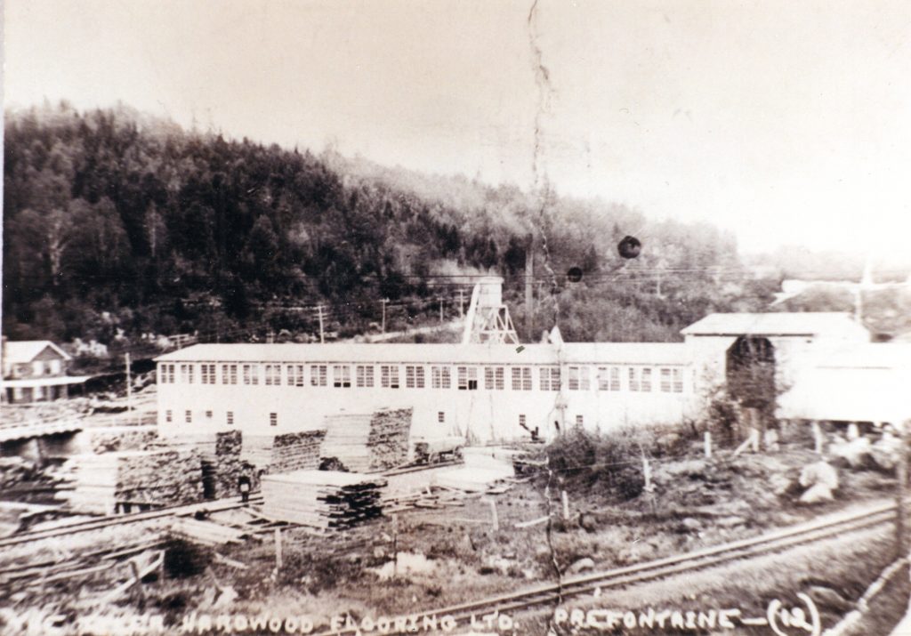 Old photograph showing the piles of lumber stacked near the railway lines and the Tyler Hardwood Flooring Wood Mills at Préfontaine in 1923.
