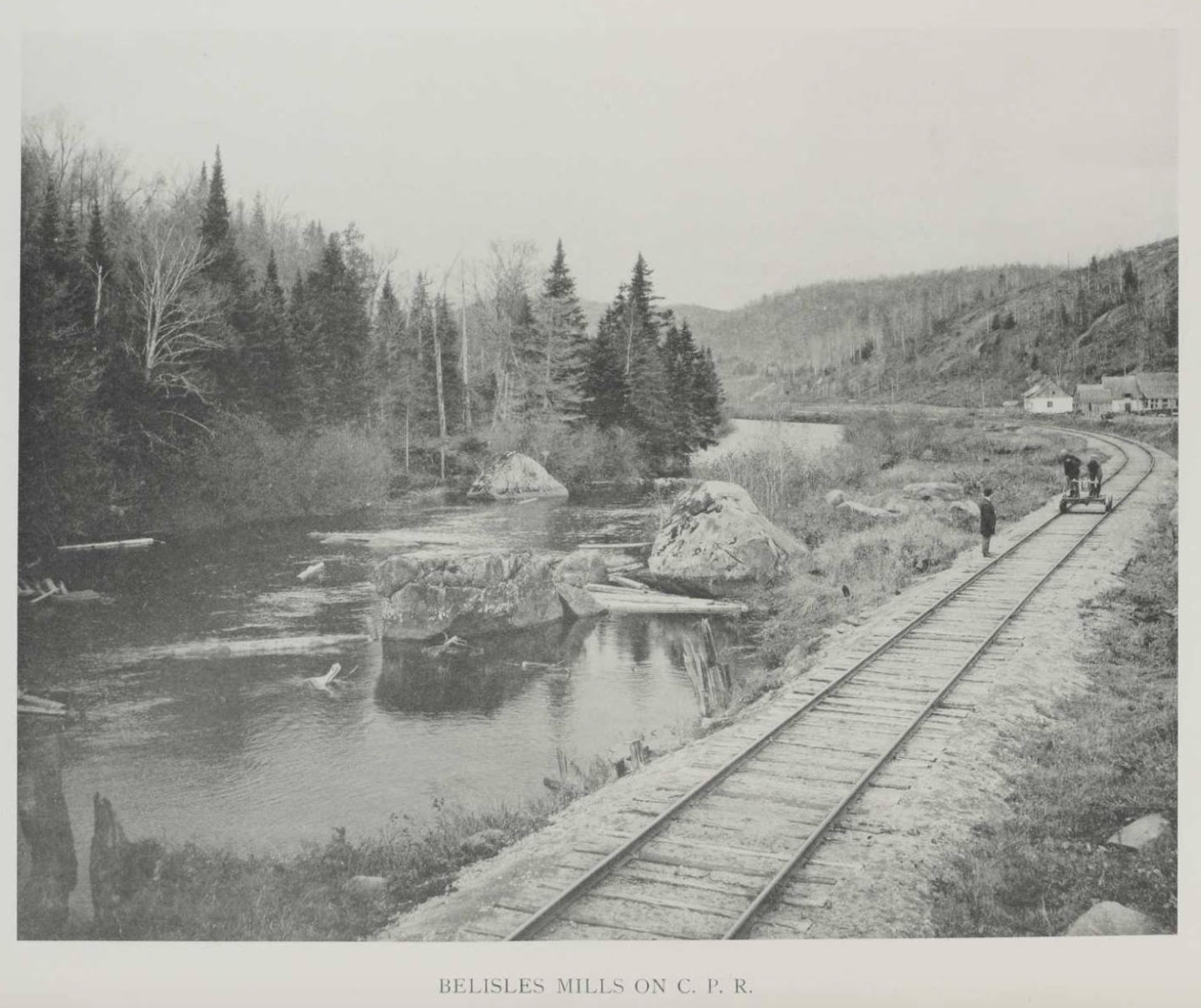 Three men on the railway tracks beside the North River, in the countryside near Val-David village. One man is standing next to the tracks, while the other two are operating a handcar, a rail vehicle used to inspect the tracks.