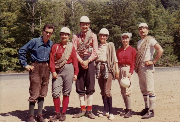 A group of six climbers, both men and women, standing with helmets and ropes on a forest road.