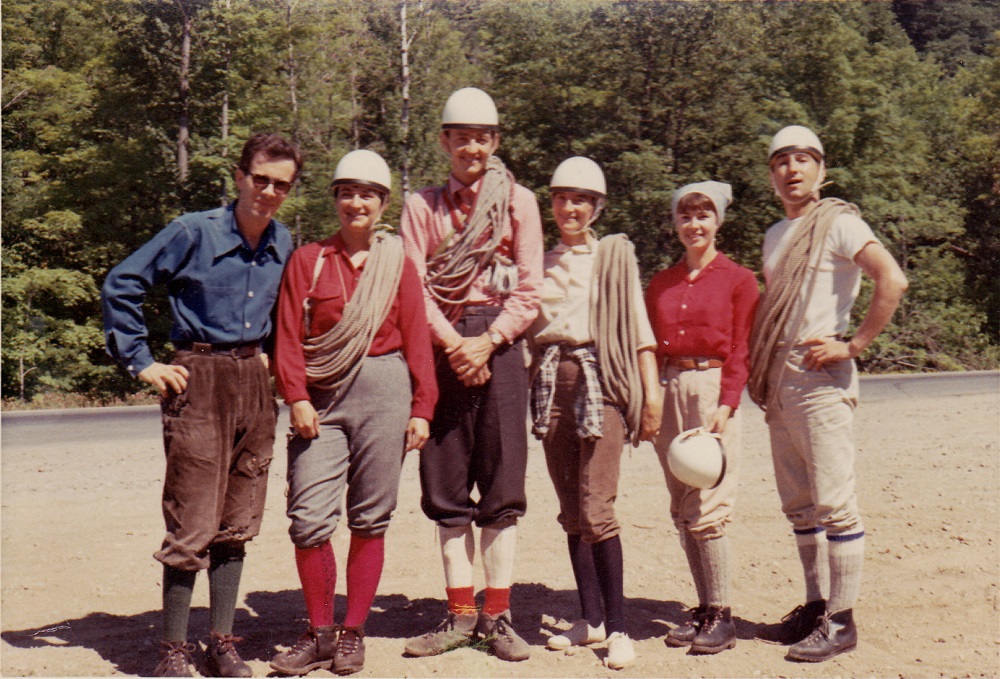 A group of six climbers, both men and women, standing with helmets and ropes on a forest road.