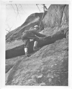 Two climbers linked by a rope, one already at the summit of the rock face.